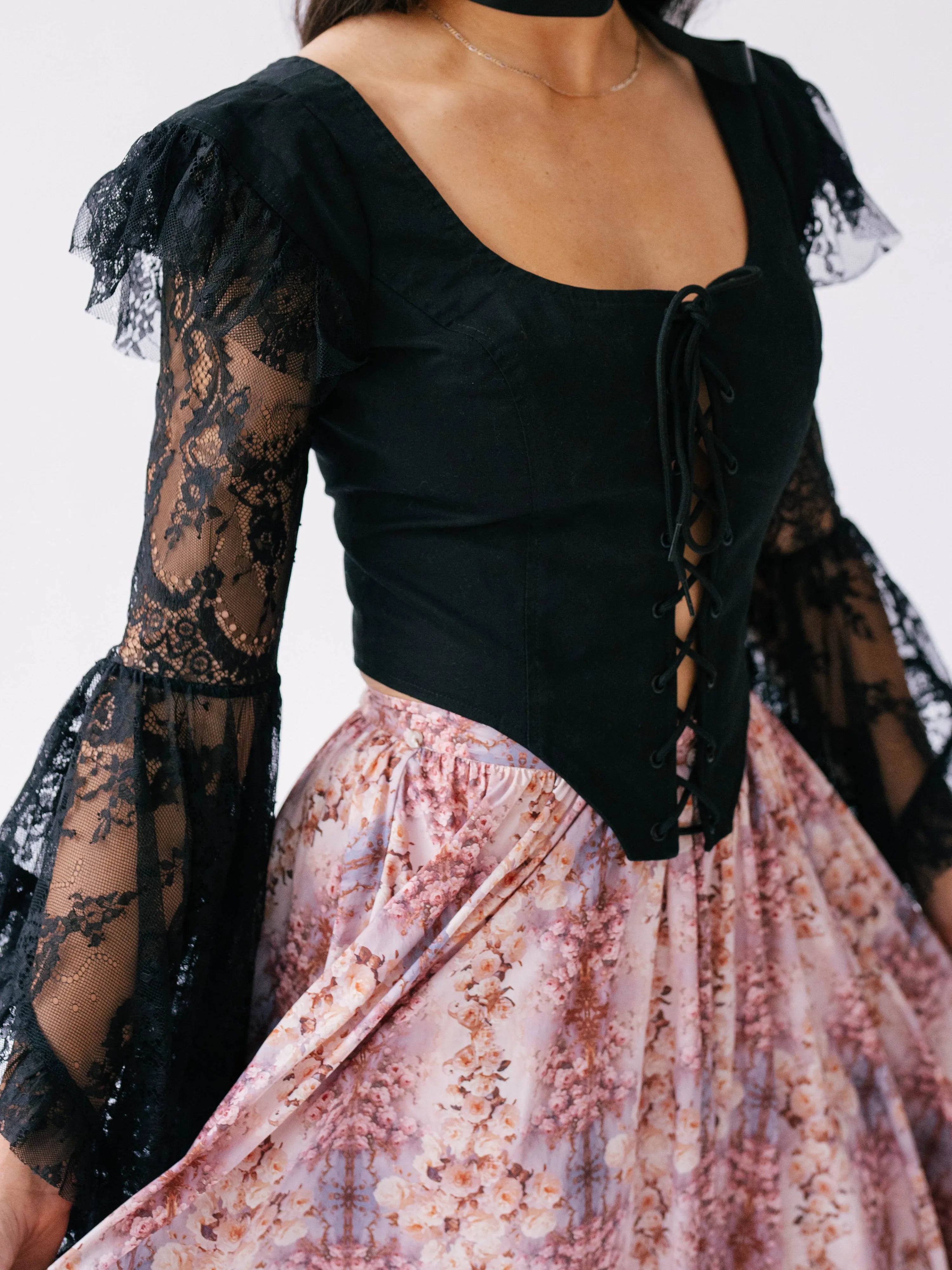 A black lace-sleeved corset top paired with a pink floral bustle skirt.