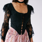 Black lace-sleeved corset top paired with a pink floral skirt. This top is called The Guineveres Revenge Lace Corset Top.
