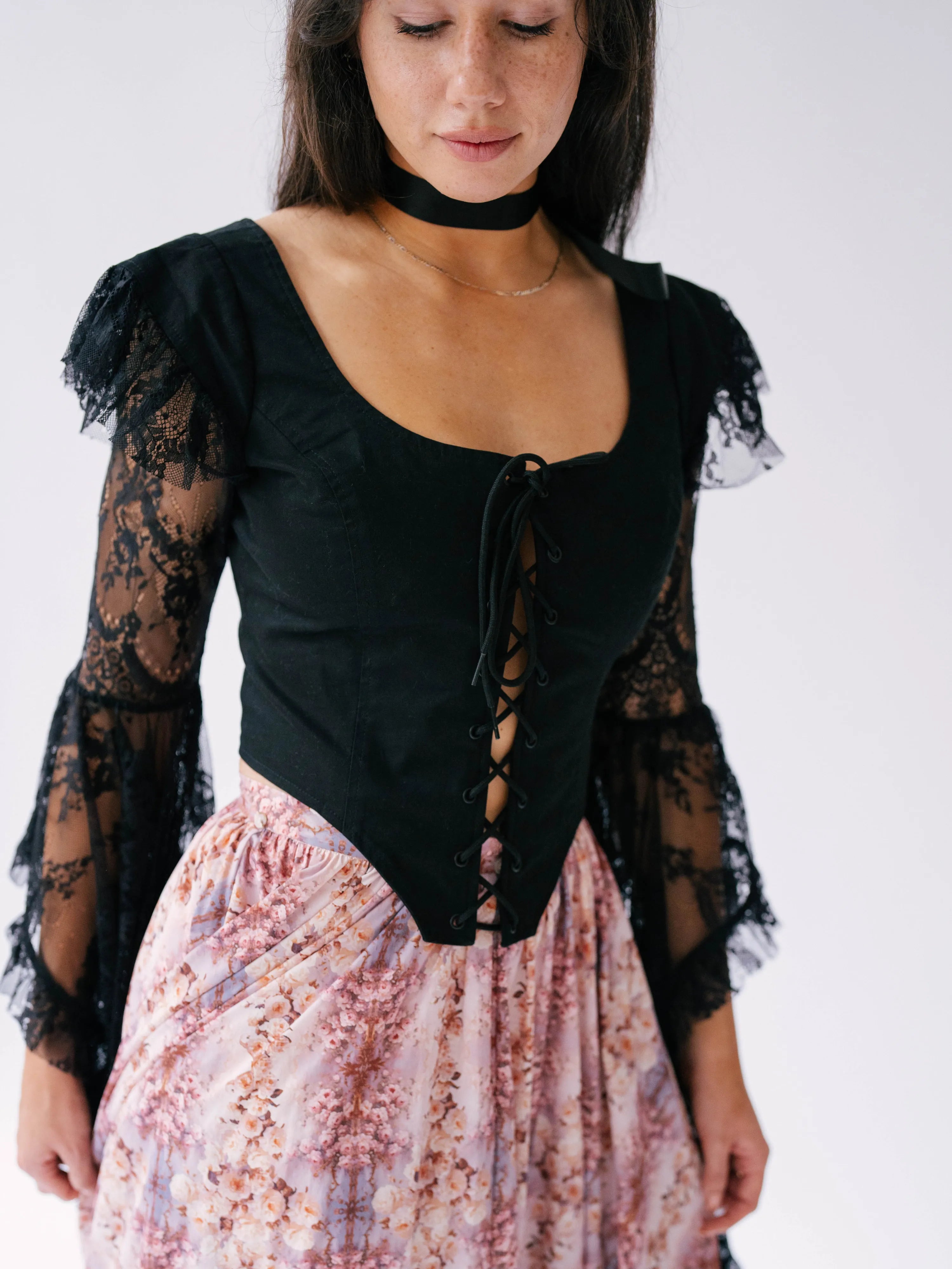 Black lace-sleeved corset top paired with a pink floral skirt. This top is called The Guineveres Revenge Lace Corset Top.