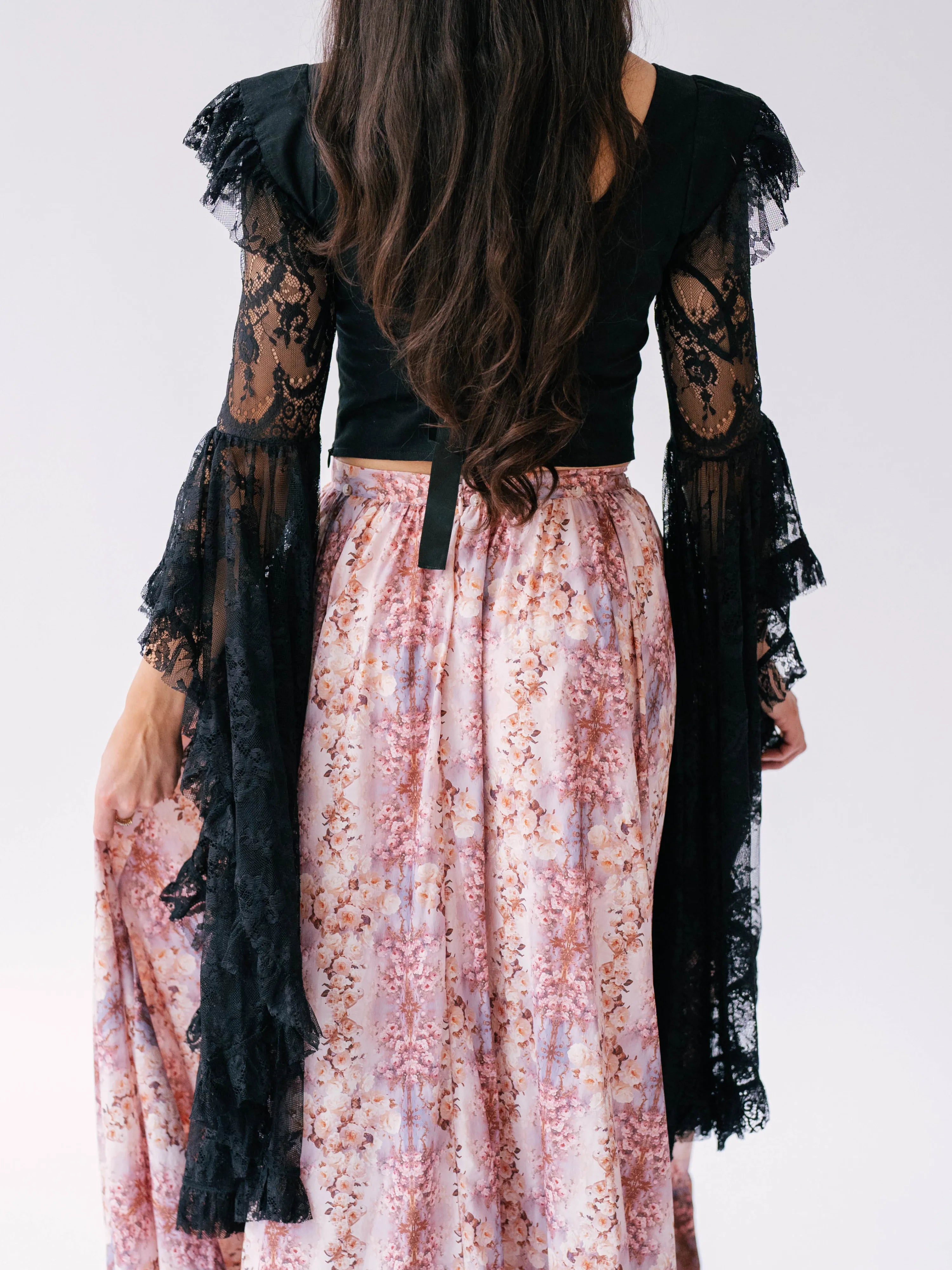 Long-sleeved black lace corset top paired with a pink floral maxi skirt that bustles.