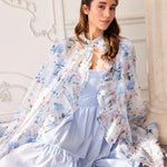 A floor length organza cape with a light pink and blue floral print over top a light blue corset midi dress. 