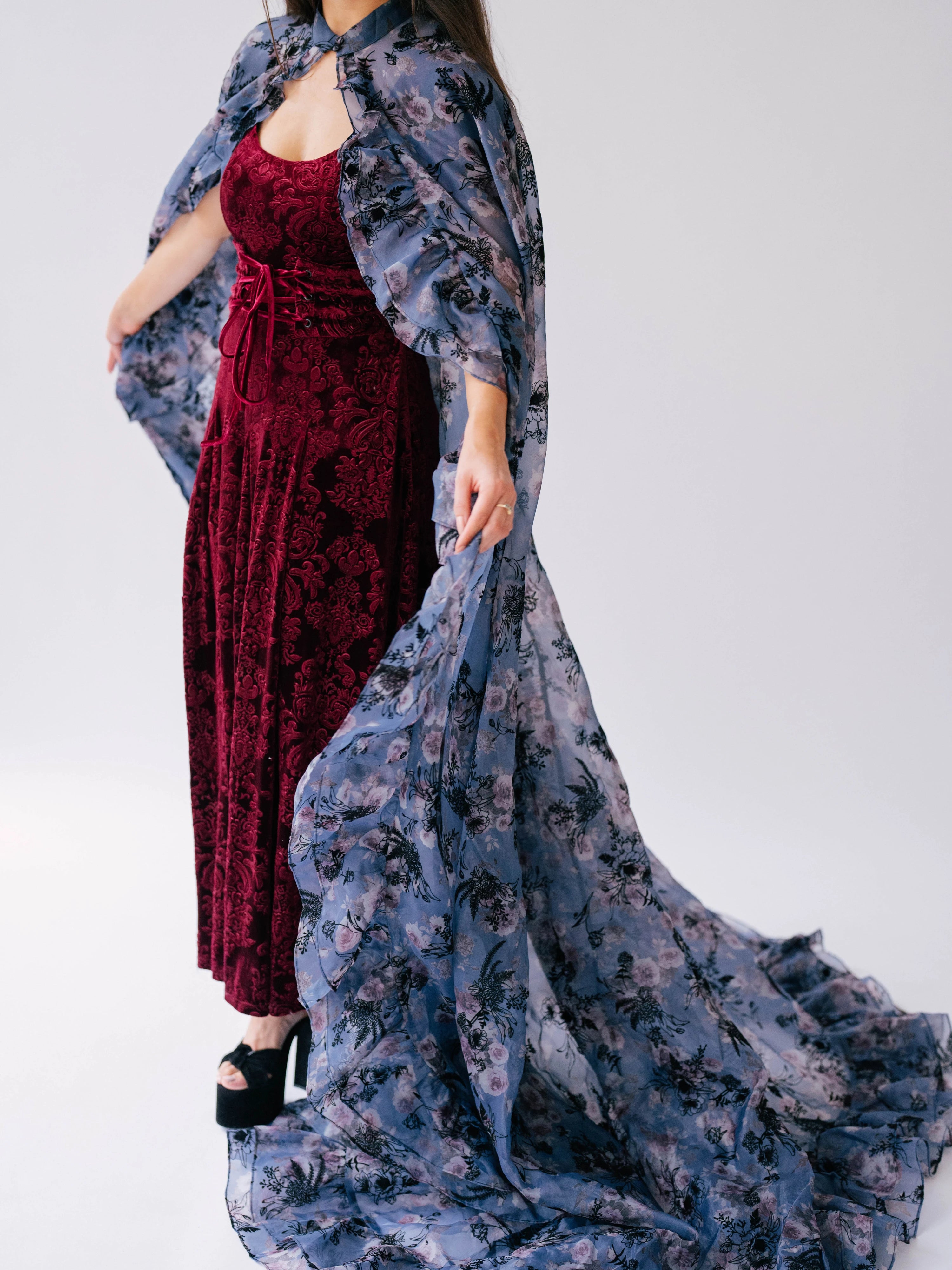 Burgundy velvet dress paired with a flowing floor length cape designed with a blue and purple floral print.