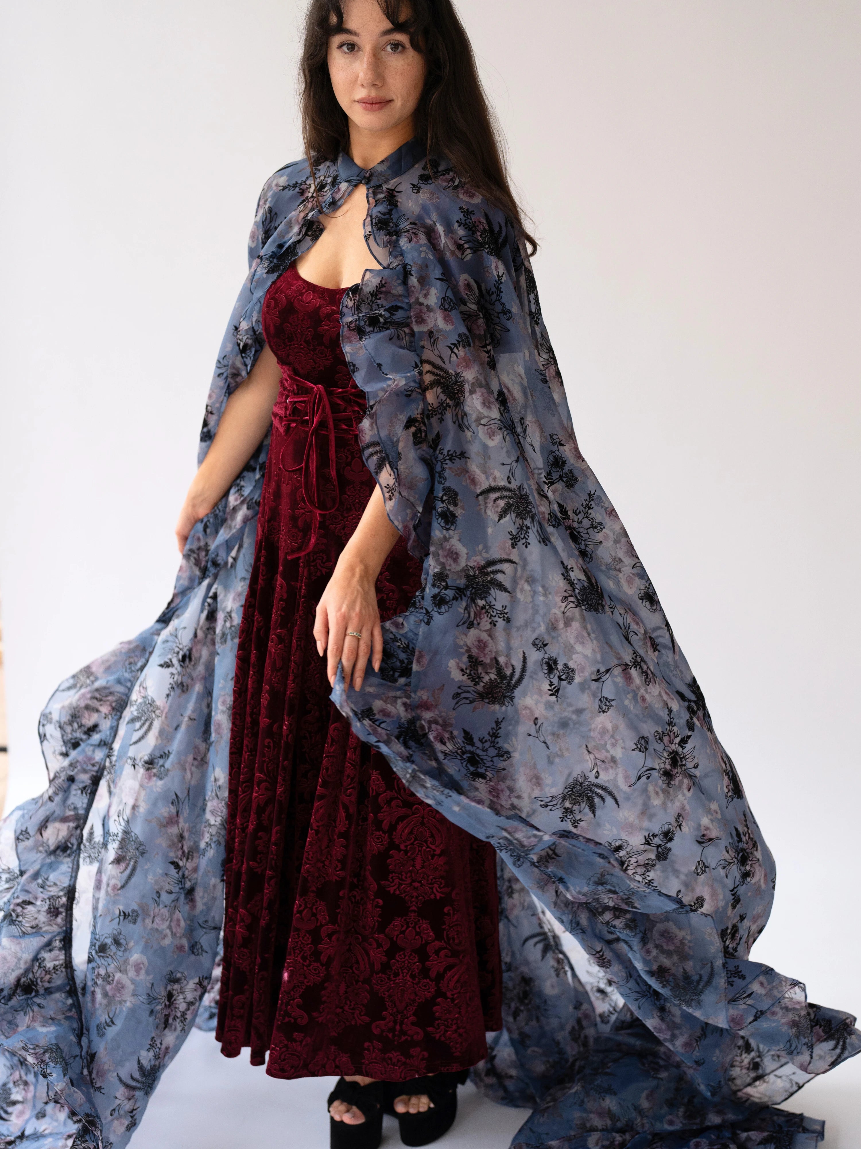 A flowing floral print organza cape worn over a red velvet dress.