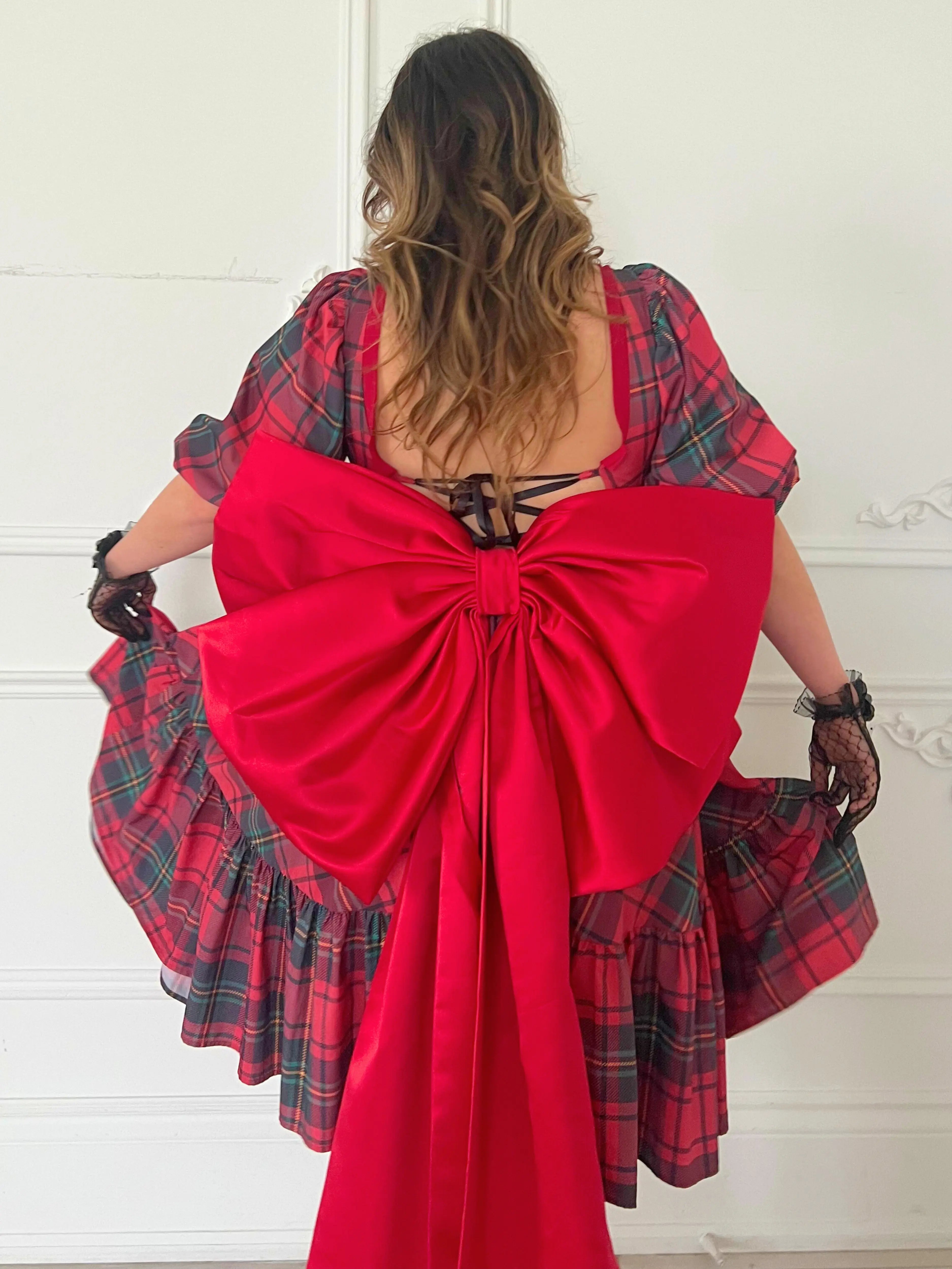 A plaid corset midi dress with a dramatic red bow belt tied at the back.