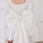 White satin bow belt adorning the back of a white mini dress.