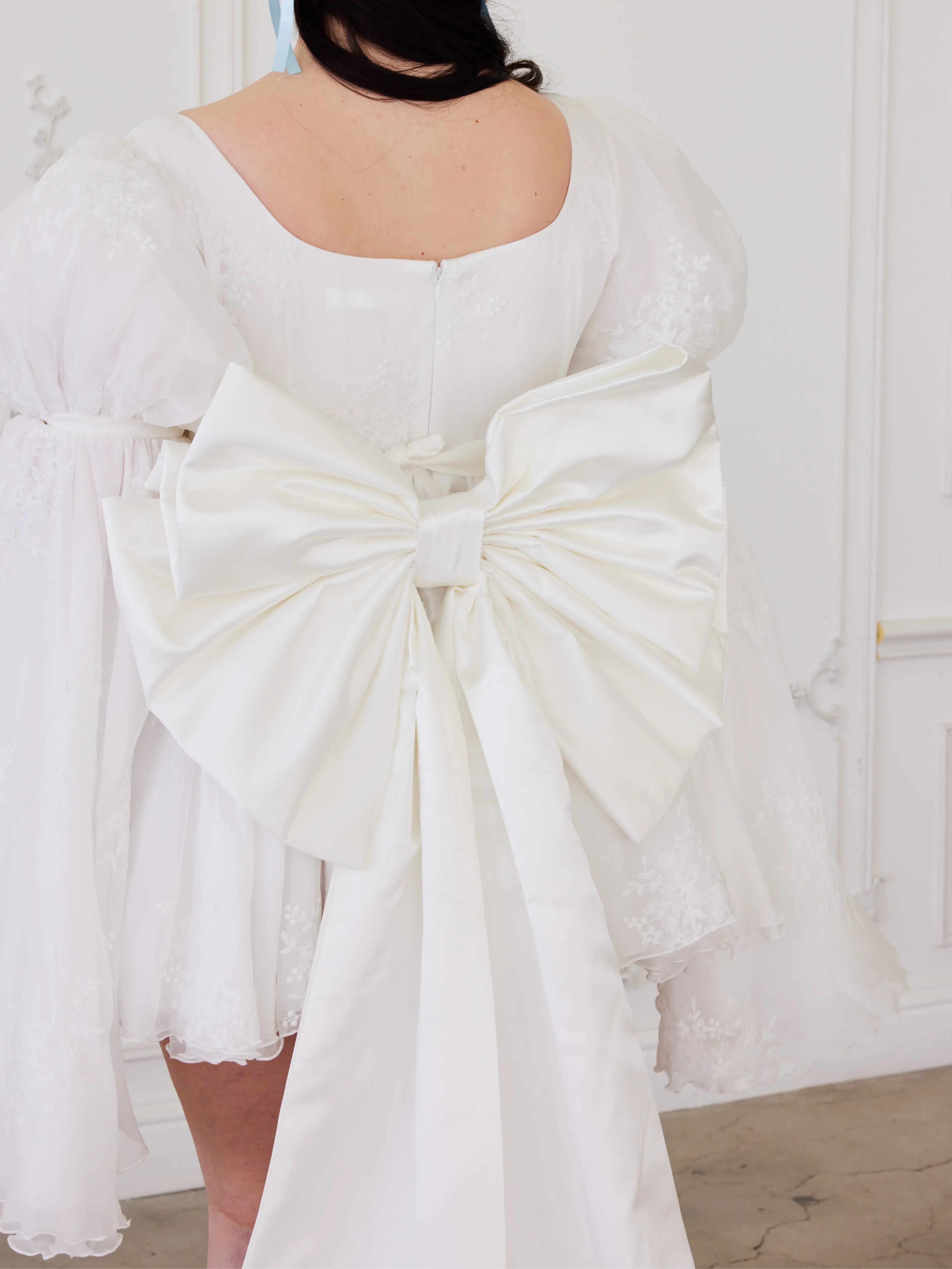 White satin bow belt adorning the back of a white mini dress.