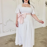 White cotton midi dress with flutter short sleeves and a pink bow sash at the waist.