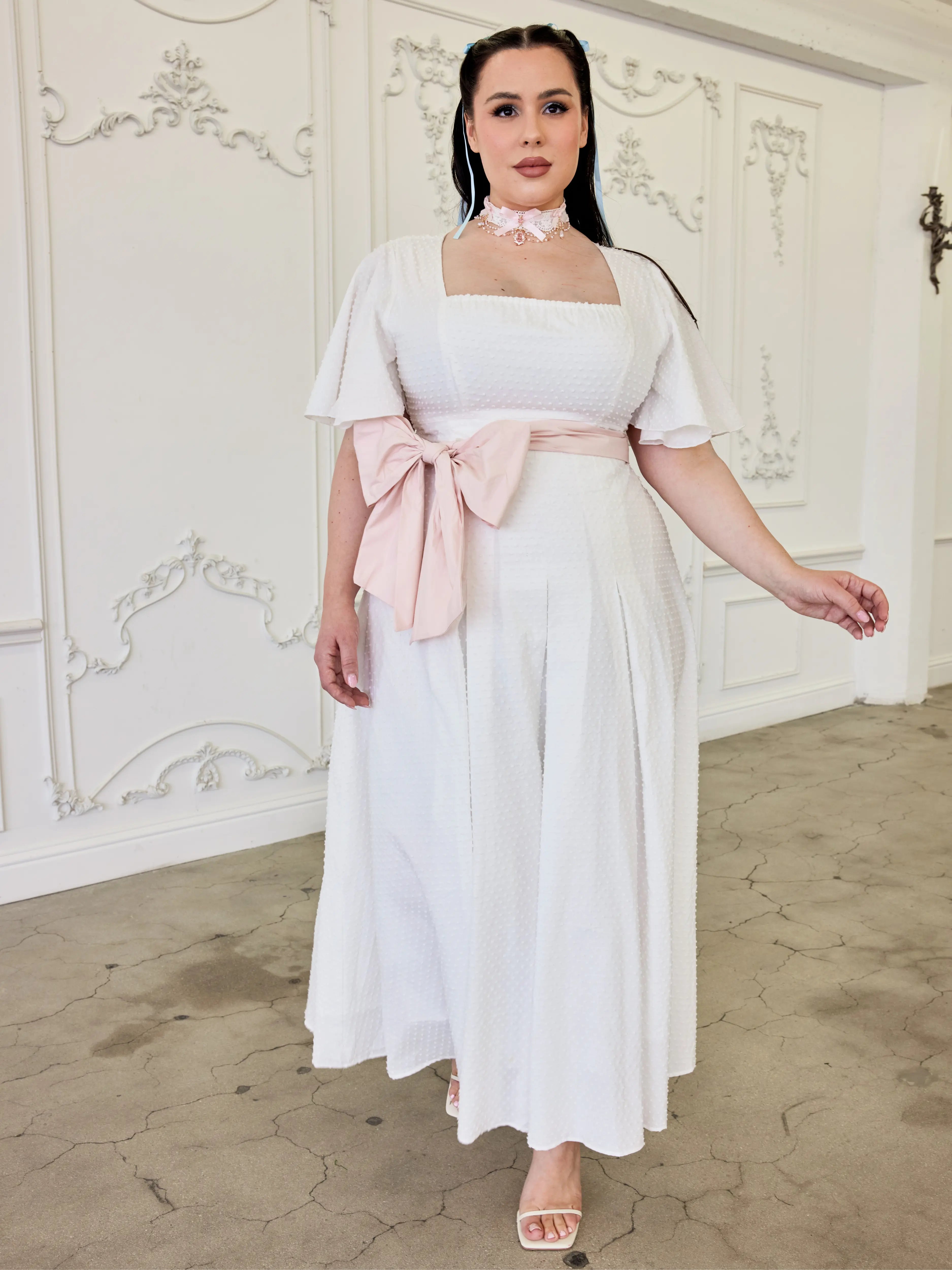 White cotton midi dress with flutter short sleeves and a pink bow sash at the waist.