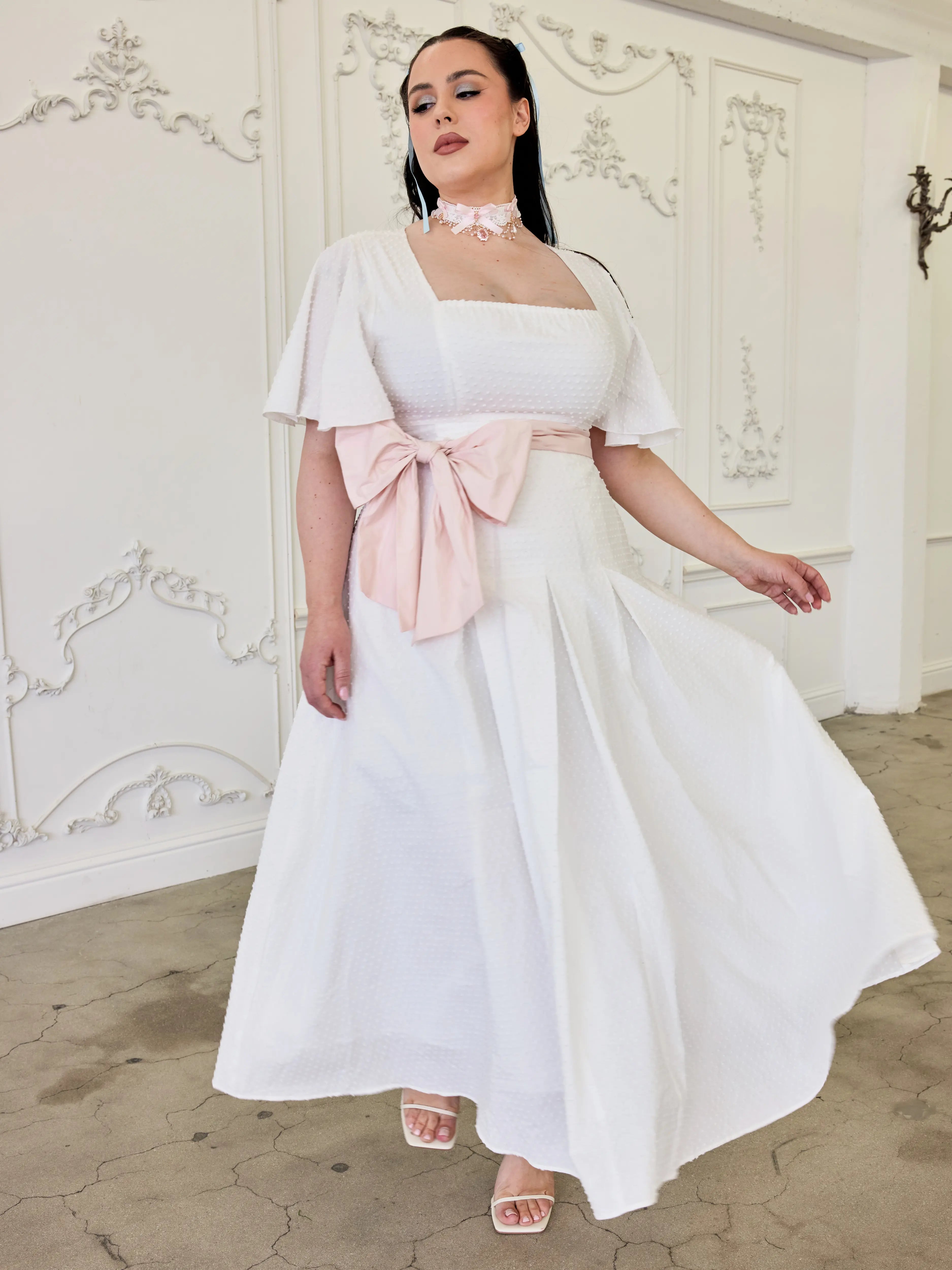 The Ivory Cloud Day Dress featuring flutter sleeves and a removable pink bow sash at the waist.