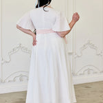 White midi dress with a pink ribbon sash tied at the waist.