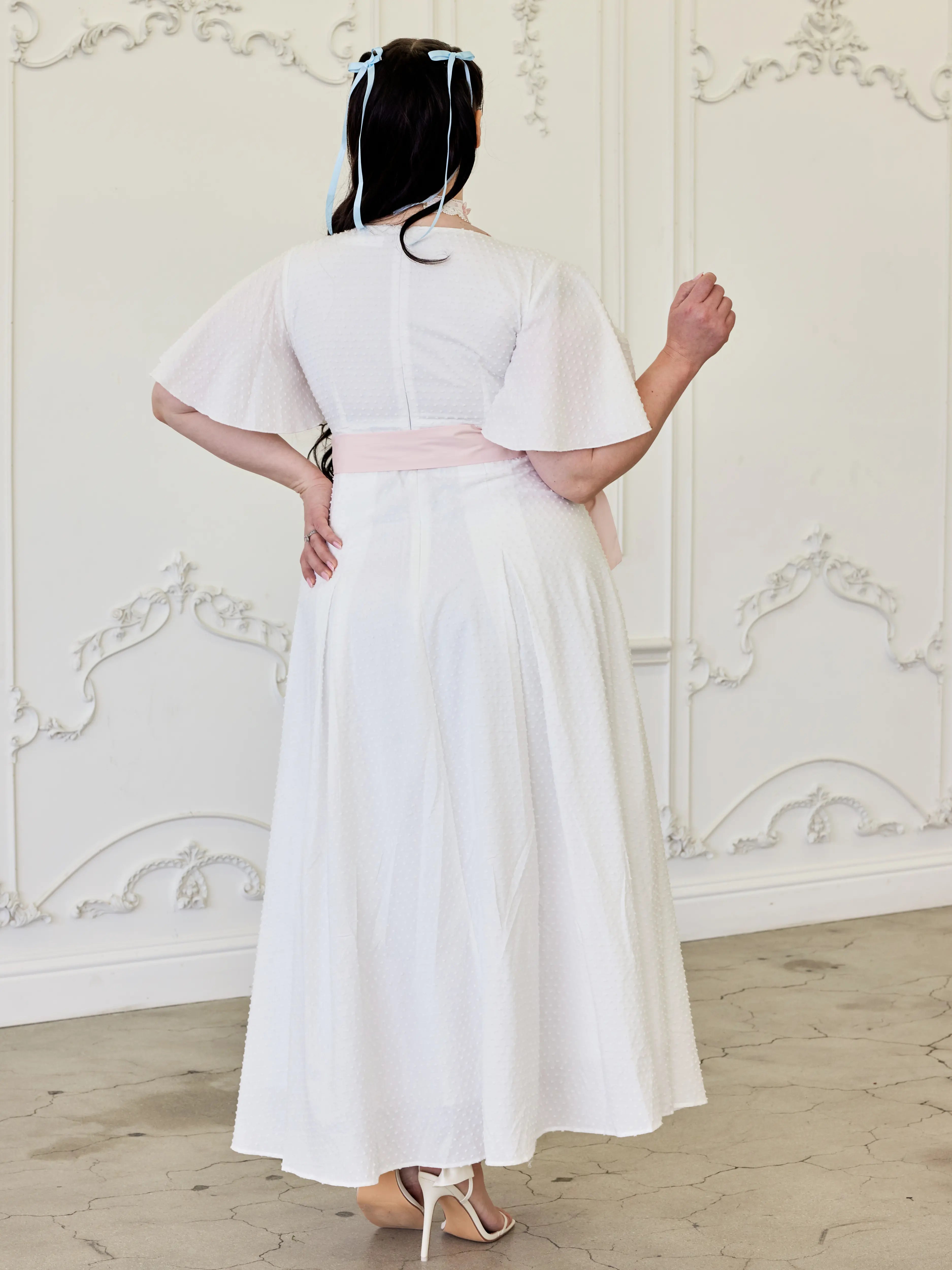 White midi dress with a pink ribbon sash tied at the waist.