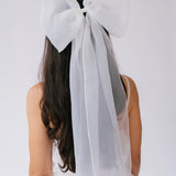 Large white bridal hair bow with flowing ribbons on dark hair for a grand bridal look