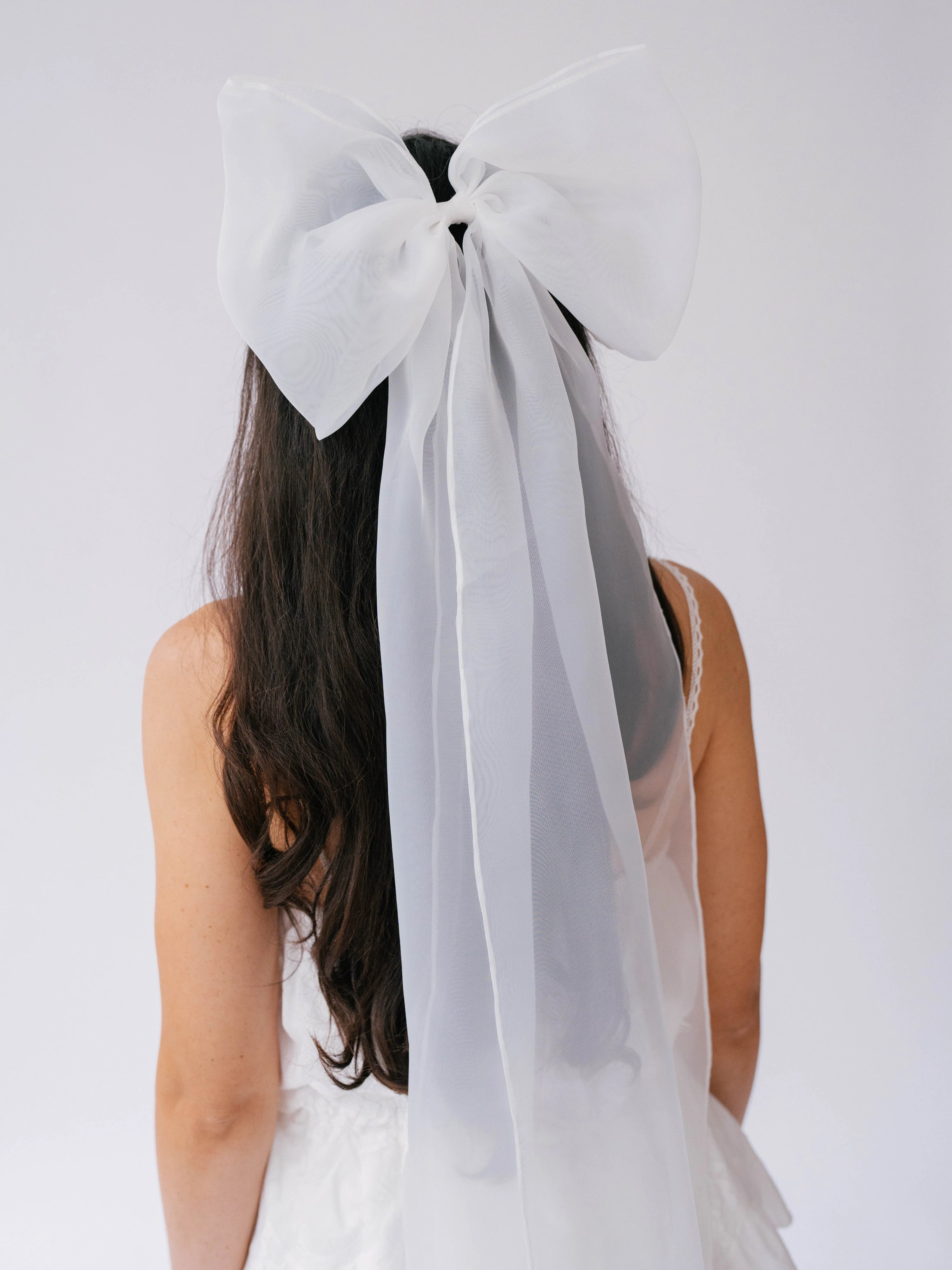 Large white bridal hair bow with flowing ribbons on dark hair for a grand bridal look