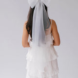 White tiered dress with grand bridal hair bow viewed from behind.