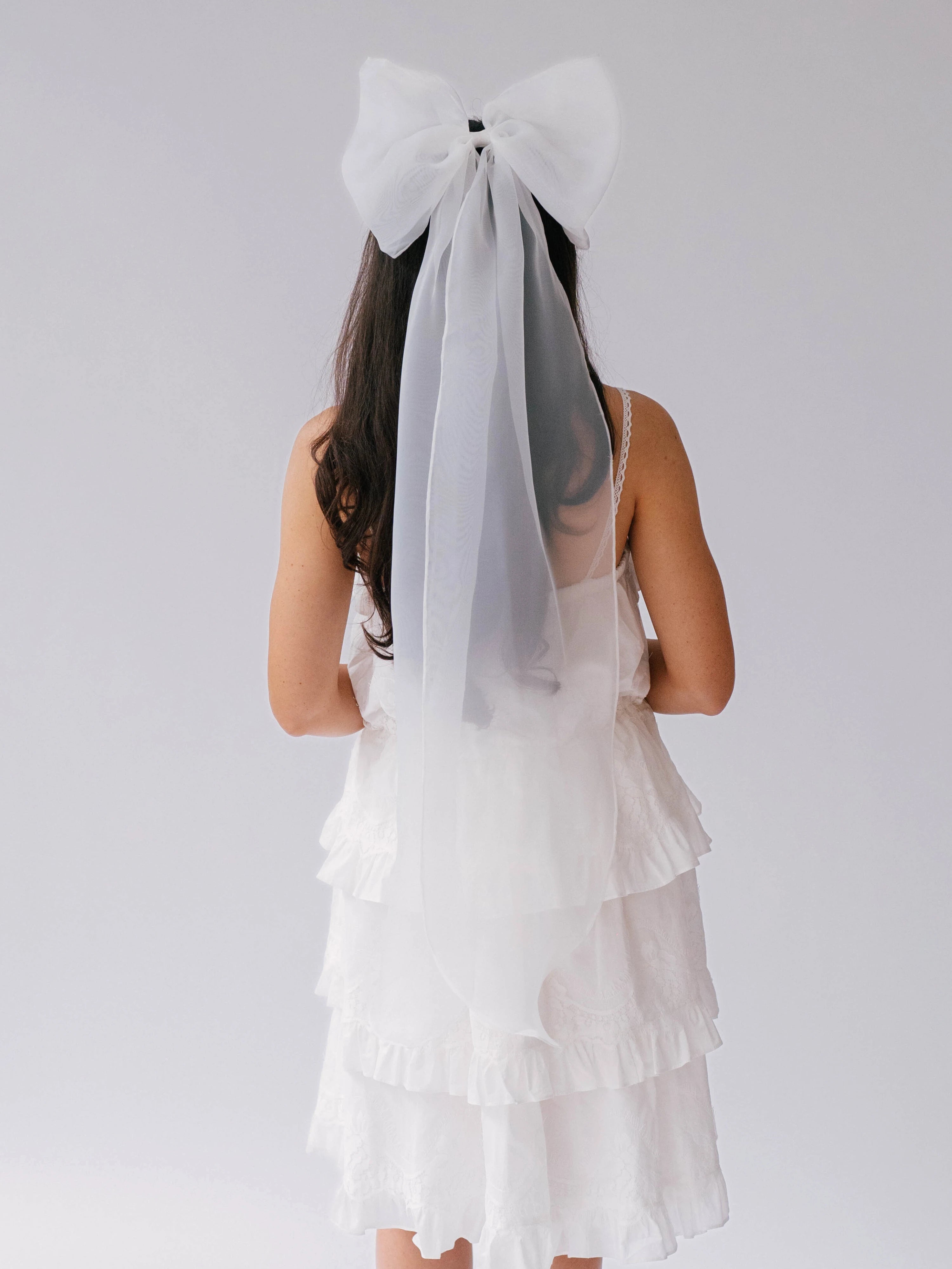 White tiered dress with grand bridal hair bow viewed from behind.