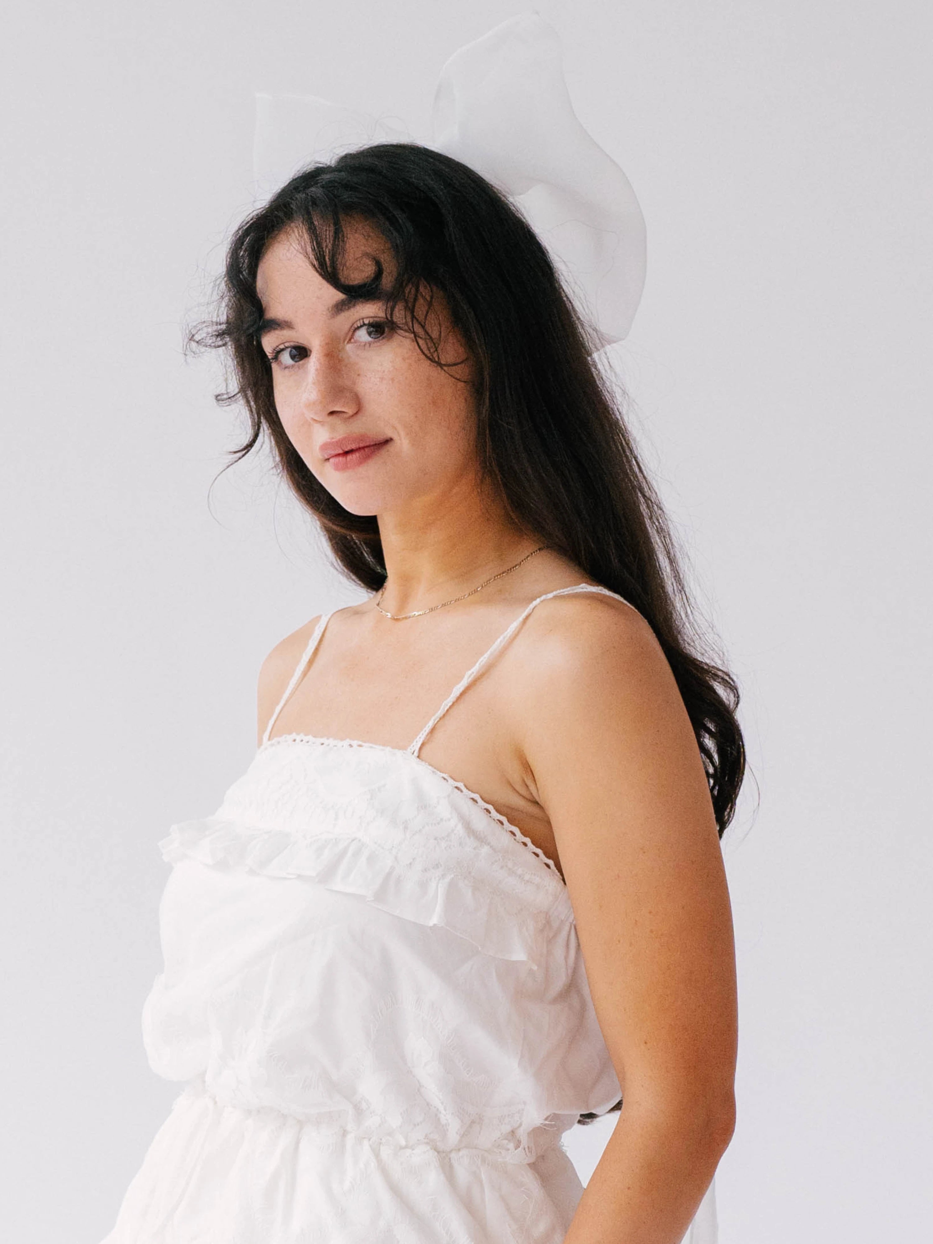 Person in white spaghetti-strap midi dress showcasing The Ivory Grand Bridal Hair Bow.