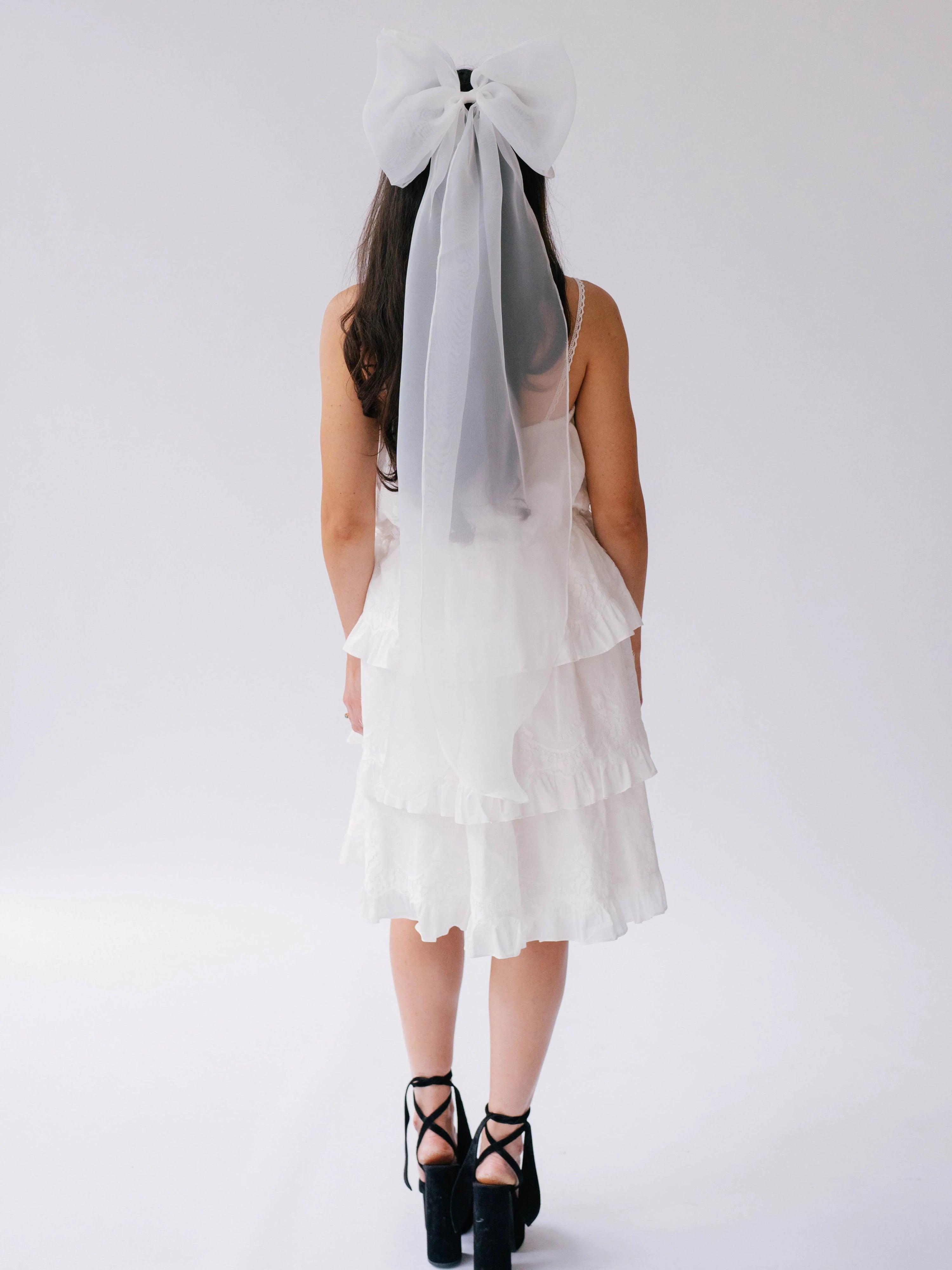 Woman wearing a white bridal mini dress with black lace-up platform shoes, and Ivory Grand Bridal Hair Bow viewed from the back.