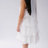 White ruffled dress with tiered layers and The Ivory Grand Bridal Hair Bow viewed from the side.