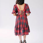 Red plaid holiday midi dress with puff sleeves, corset back, and tiered skirt paired with black platform sandals.