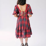 Red plaid holiday midi dress with puff sleeves, corset back, and tiered skirt paired with black platform sandals.