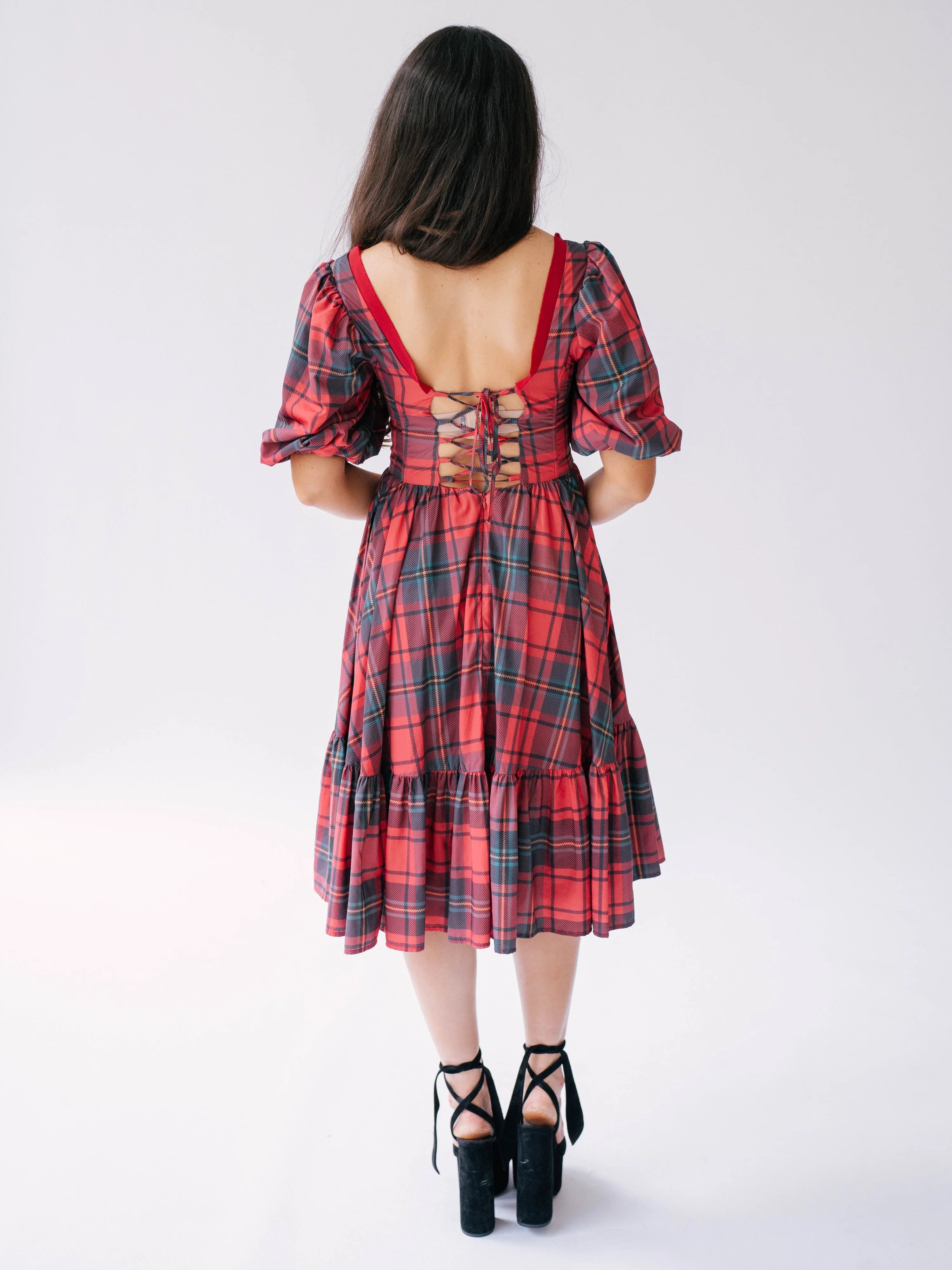 Red plaid holiday midi dress with puff sleeves, corset back, and tiered skirt paired with black platform sandals.