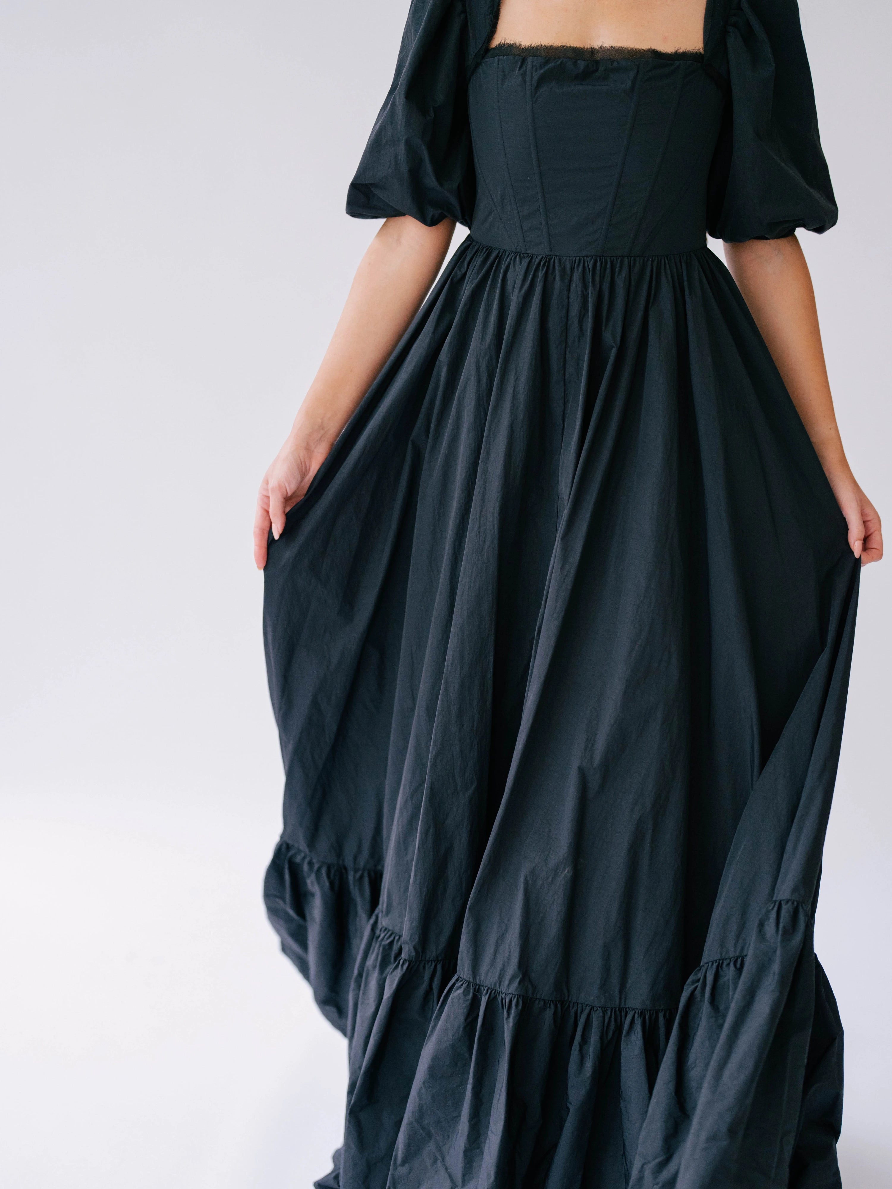 Black taffeta corset renaissance gown with puff sleeves and a tiered, flowing skirt.