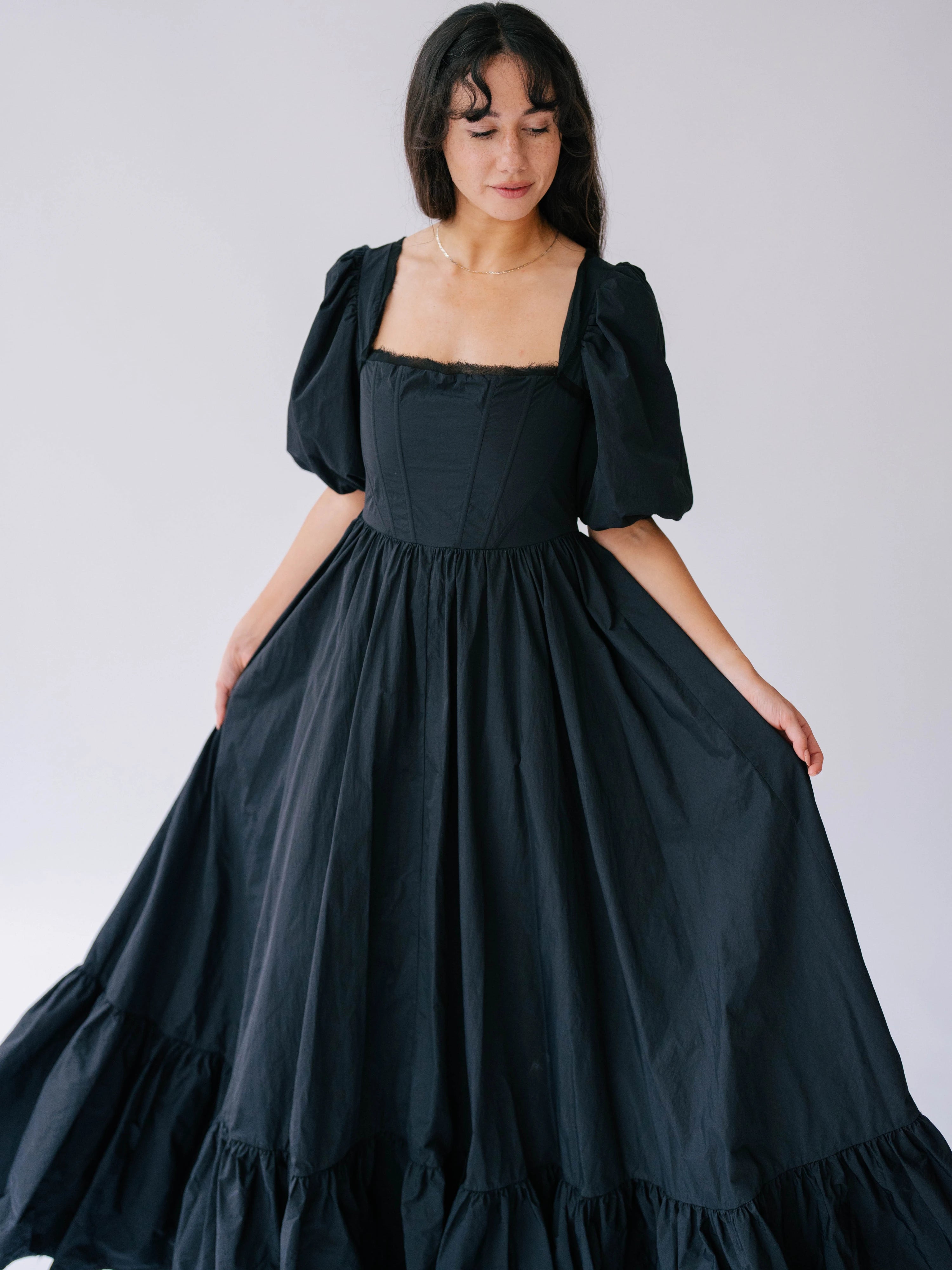 The Josephine Renaissance Gown is a Black taffeta corset dress with puff sleeves and a ruffled hem.