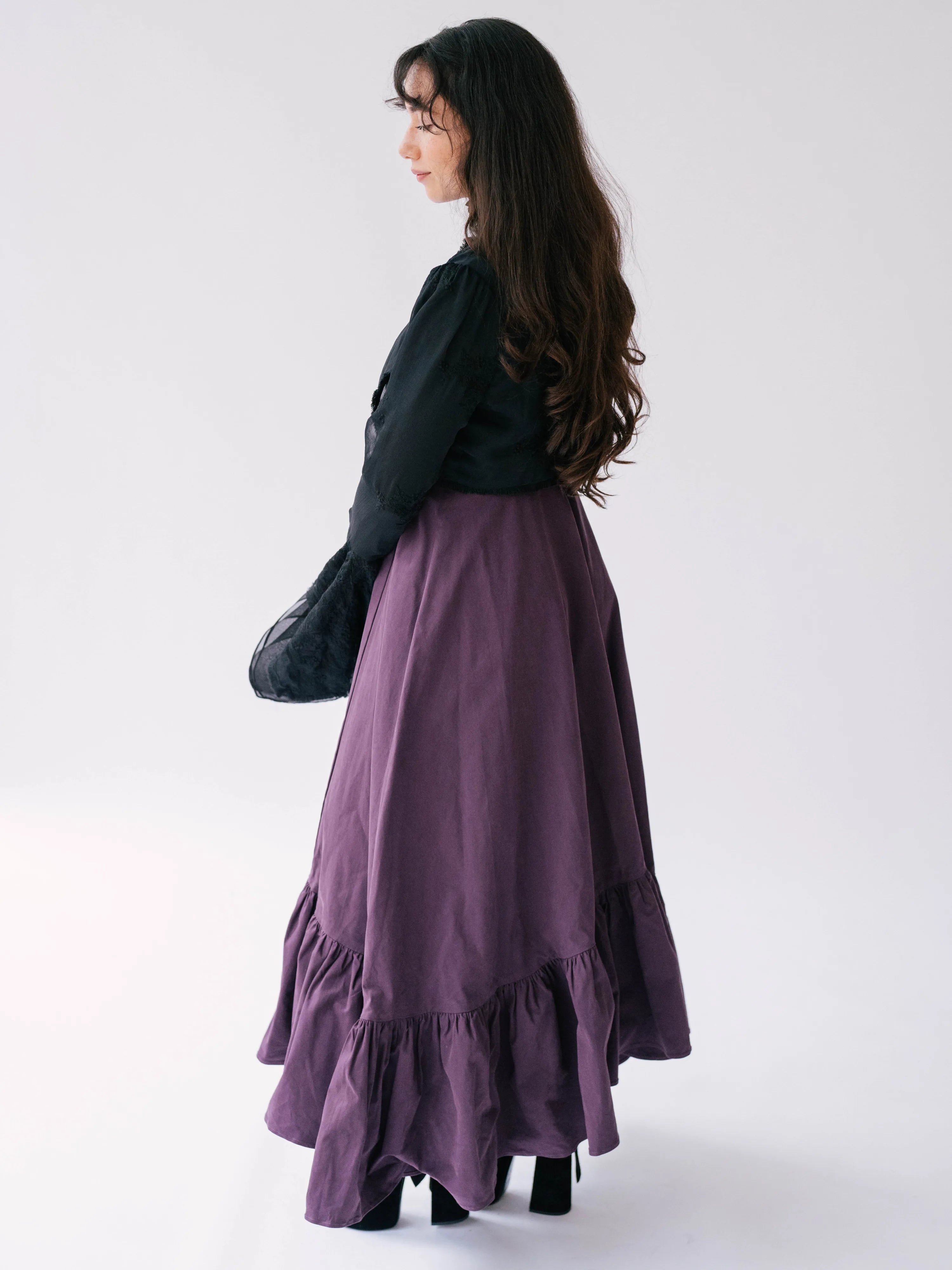 A flowing purple midi dress with ruffled hem detailing underneath The Lady Elizabeth Midnight Black Victorian Jacket.