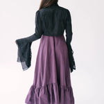 A black lace bolero jacket shown from behind overtop a purple midi dress.