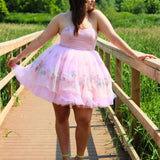 Pink tulle party dress with empire bodice, worn by a woman on a wooden pier in a forest for a fairytale look.