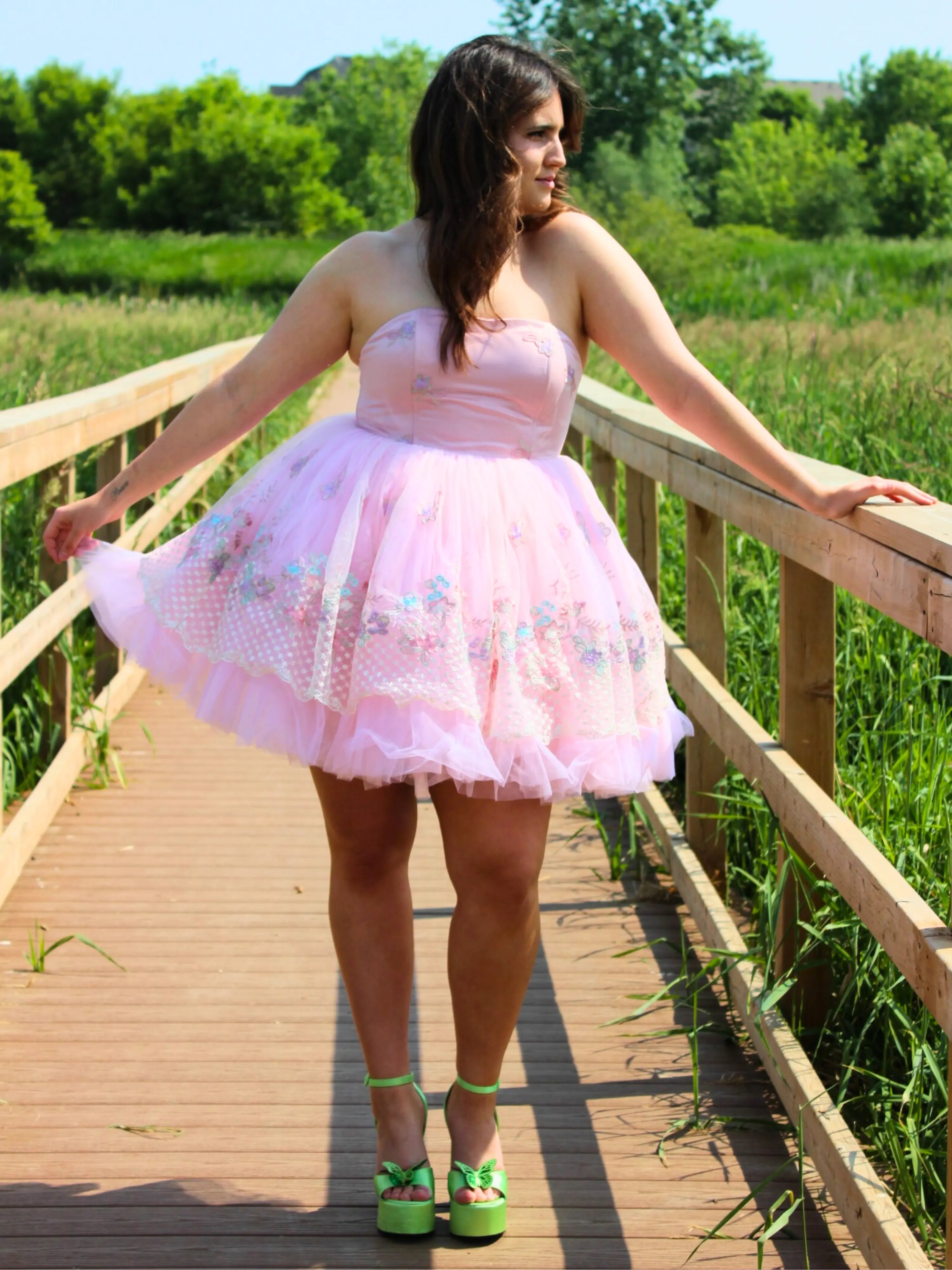 Pink tulle party dress with empire bodice, worn by a woman on a wooden pier in a forest for a fairytale look.