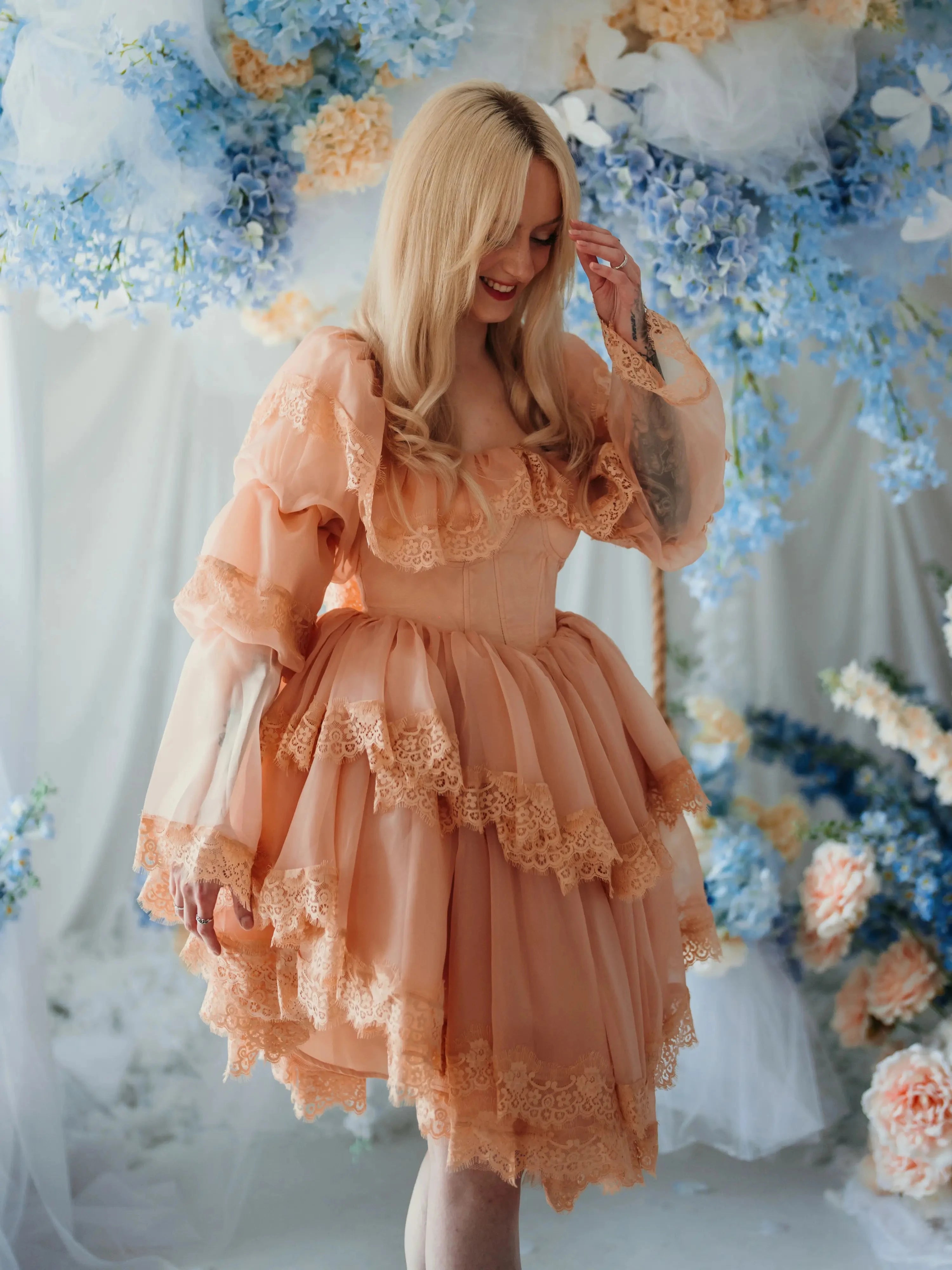 Smiling model in floral setting wearing the Midnight Symphony Mini Gown, a fairytale-inspired mini dress with layered lace and puff sleeves.