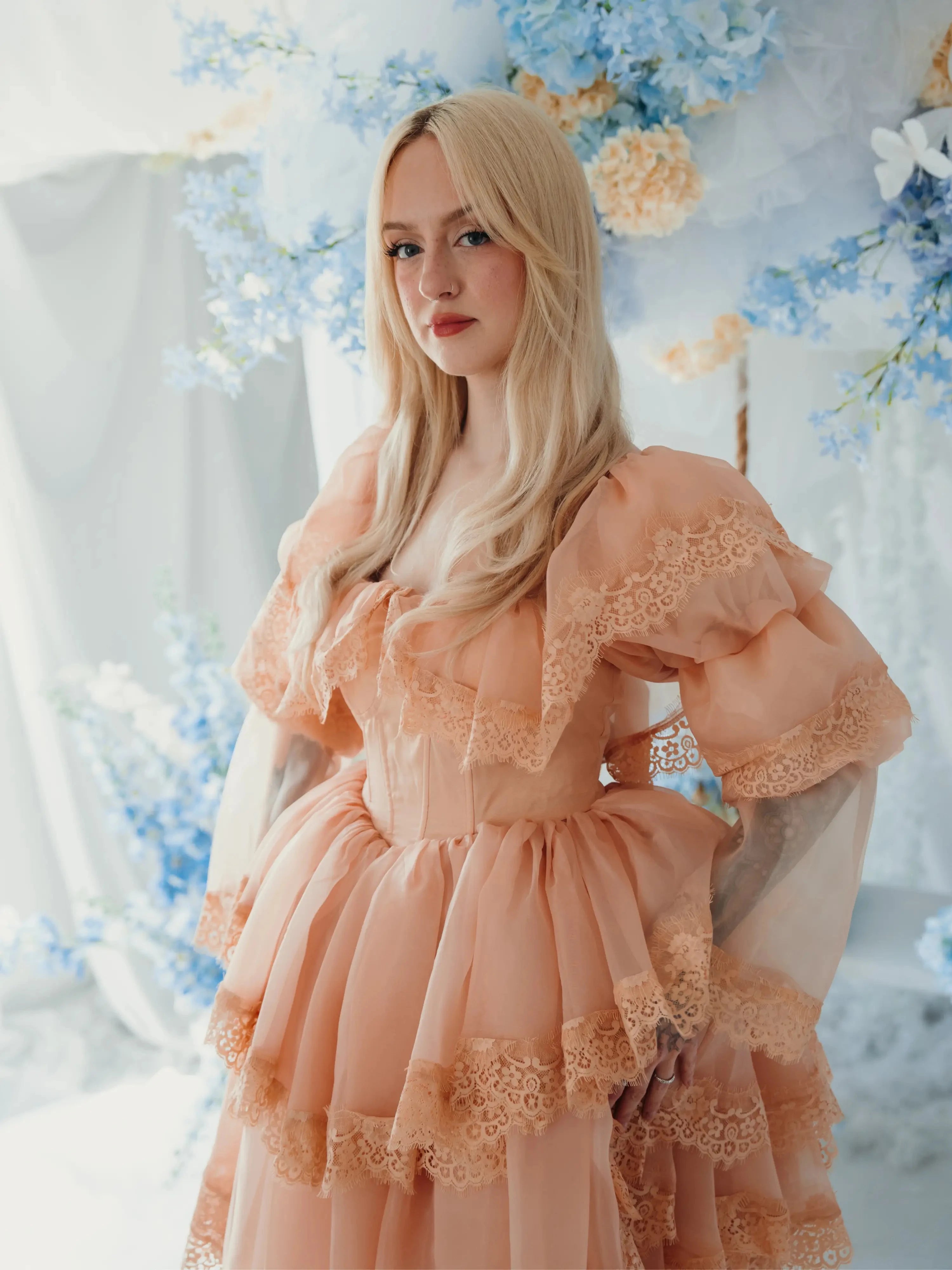 Model in floral backdrop wearing the Midnight Symphony Mini Gown, highlighting its vintage-inspired silhouette and lace detailing.
