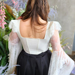 Woman in The Guinevere Corset Top with lace sleeves and dark skirt, showcasing corset features from the back.