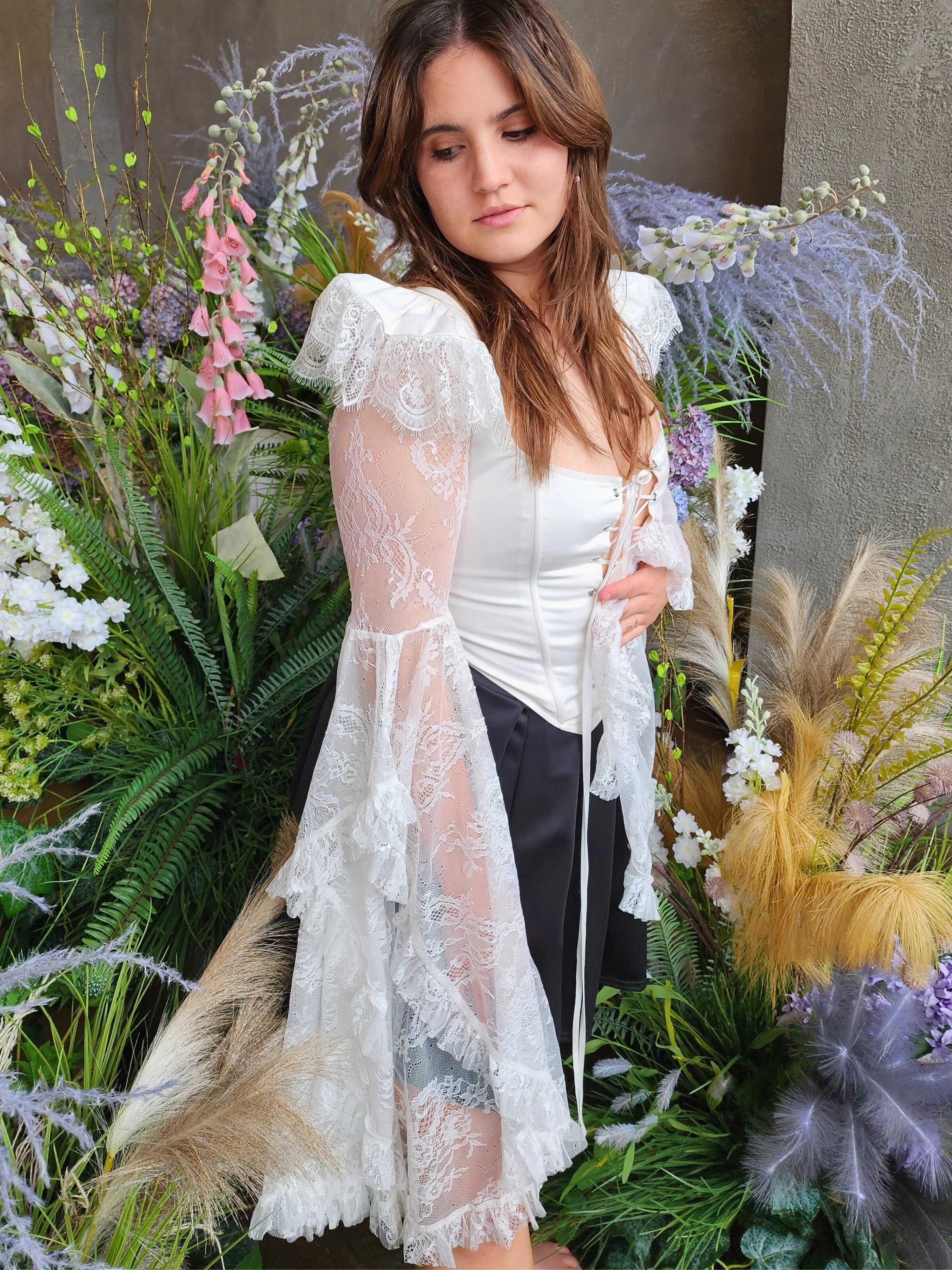 Woman in a white lace a white lace corset called The Guinevere Corset Top crafted with bell sleeves and synthetic whale boning.