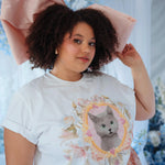 Model in The Princess Kitten Tee with oversized pink bow and floral skirt, emphasizing the tee’s playful and artistic kitten print.
