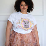 The Princess Kitten Tee styled casually with a floral skirt, highlighting the central kitten artwork and rolled sleeves for a relaxed fit.