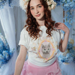 Model wearing The Princess Kitten Tee in a floral-themed setting, styled with a flower crown and pink ruffle skirt for a whimsical look.