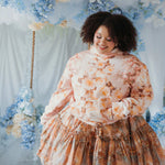 The Twilight Bloom Sleeper Hoodie paired with a floral skirt, modeled in a pastel floral backdrop. Oversized fit ideal for comfort and charm.