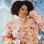 The Twilight Bloom Sleeper Hoodie in soft pink with peach floral print, modeled in a dreamy floral setting. Cozy oversized fit for romantic style lovers.