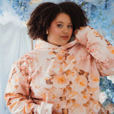 The Twilight Bloom Sleeper Hoodie in soft pink with peach floral print, modeled in a dreamy floral setting. Cozy oversized fit for romantic style lovers.