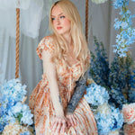 Model seated among blue hydrangeas wearing Twilight Bloom Meadow Gown, highlighting its fairytale floral design.