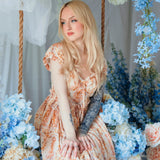 Model seated among blue hydrangeas wearing Twilight Bloom Meadow Gown, highlighting its fairytale floral design.