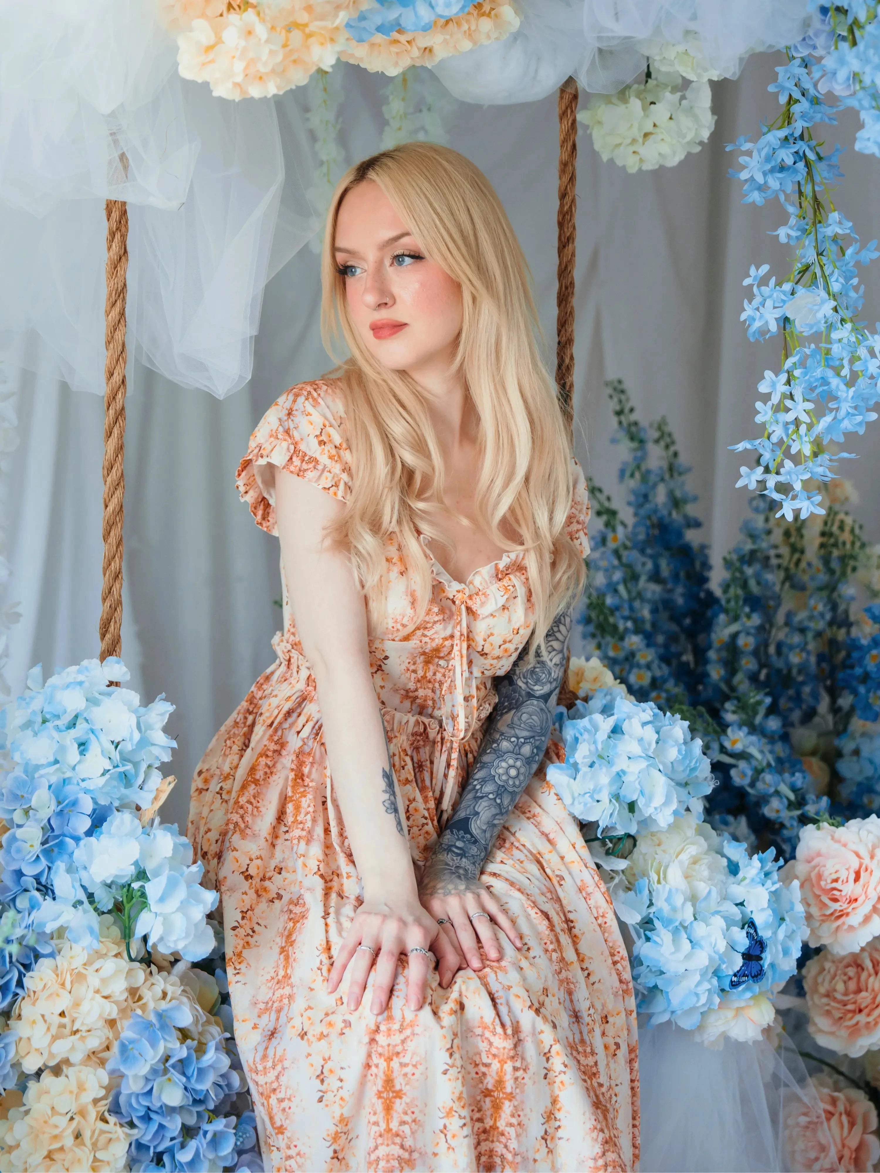 Model seated among blue hydrangeas wearing Twilight Bloom Meadow Gown, highlighting its fairytale floral design.