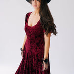 A scarlet red velvet victorian dress with a fitted bodice, floral pattern and flowing skirt.