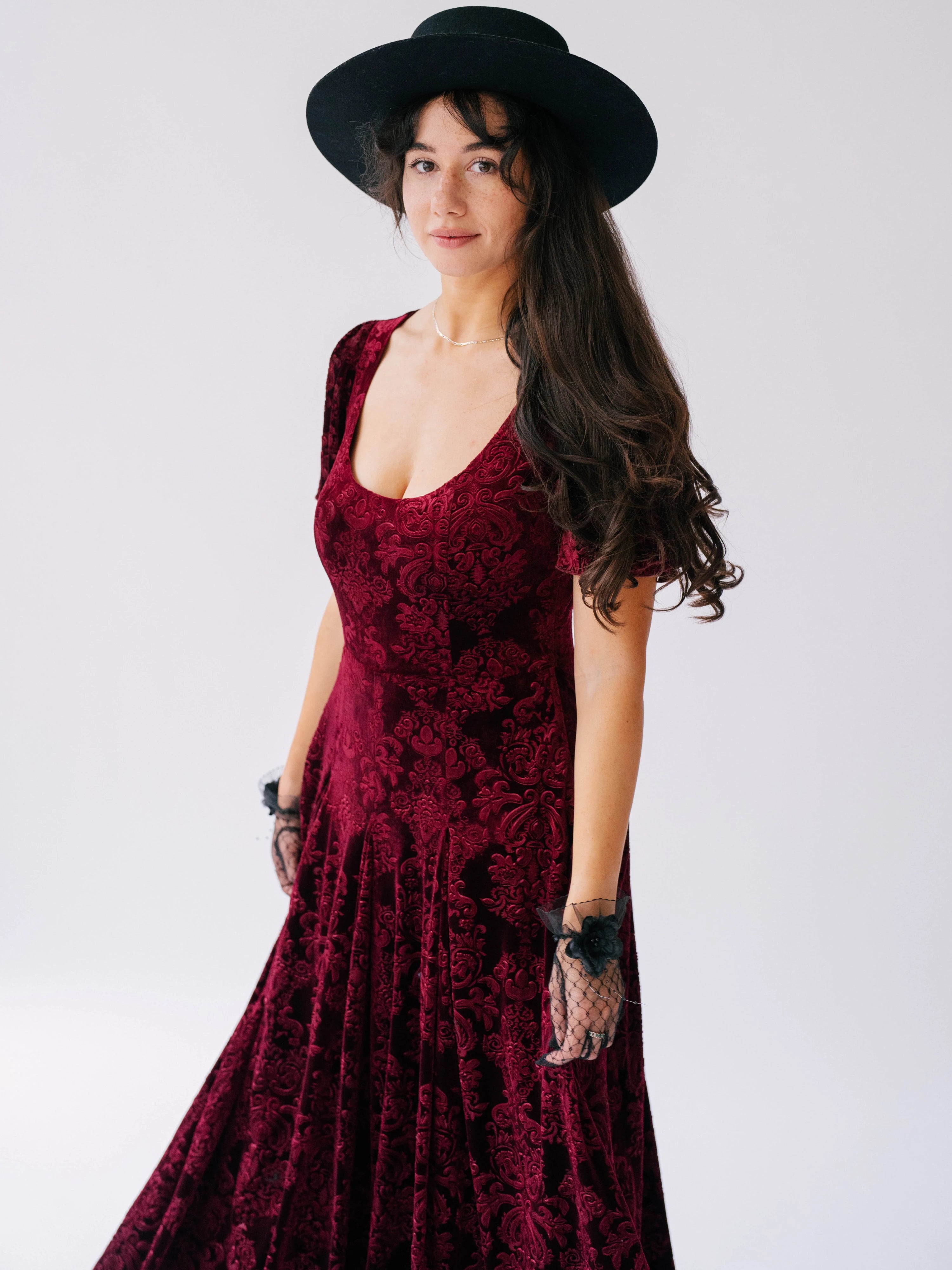 A scarlet red velvet victorian dress with a fitted bodice, floral pattern and flowing skirt.
