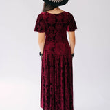 Scarlet red velvet victorian dress with delicate floral patterns worn with a black hat and platform sandals.