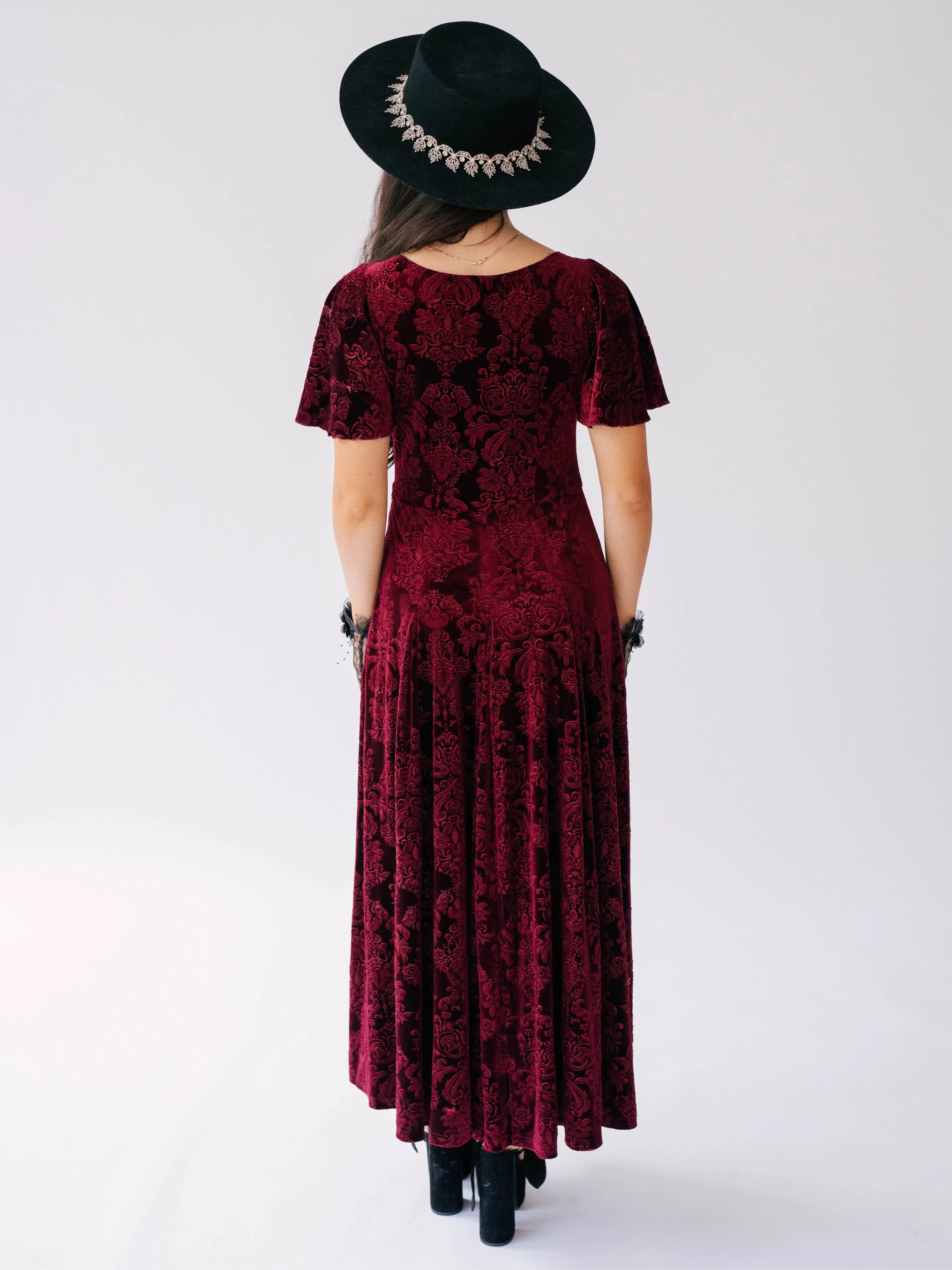 Scarlet red velvet victorian dress with delicate floral patterns worn with a black hat and platform sandals.