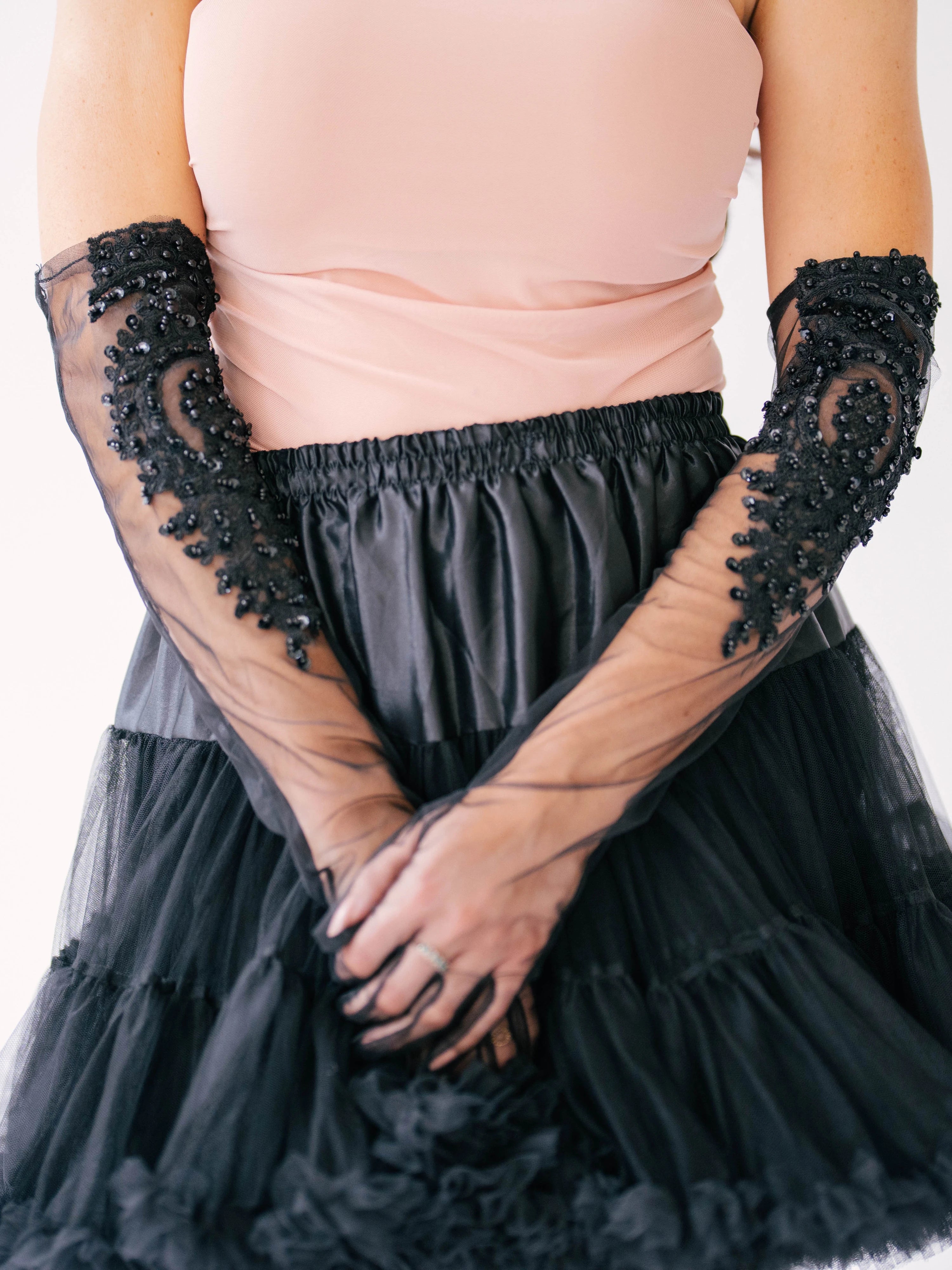 Elegant black tulle mini skirt paired with sheer lace evening gloves and a blush pink blouse.
