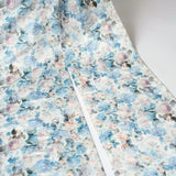 The oversized bow, zoomed in shows a floral fabric with blue and pink watercolor-style flowers on a white background. This print is called Wildbloom. 